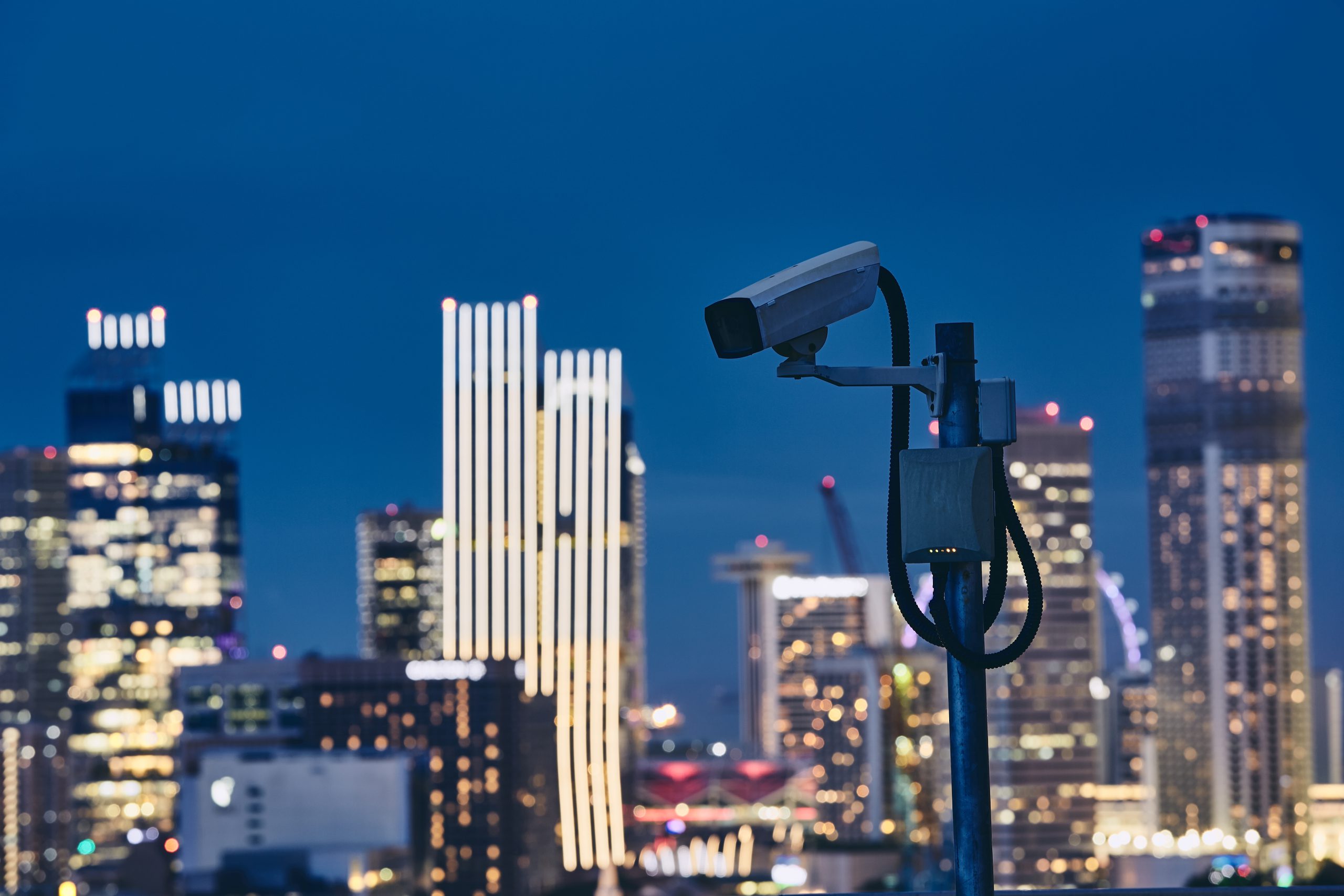 Security camera against illuminated urban skyline at night. Concept of surveillance, protection and safety.